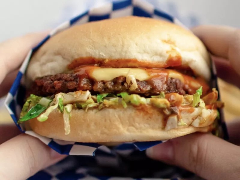 Two hands holding a Meta Burger sandwich featuring a plant-based patty and vegan cheese