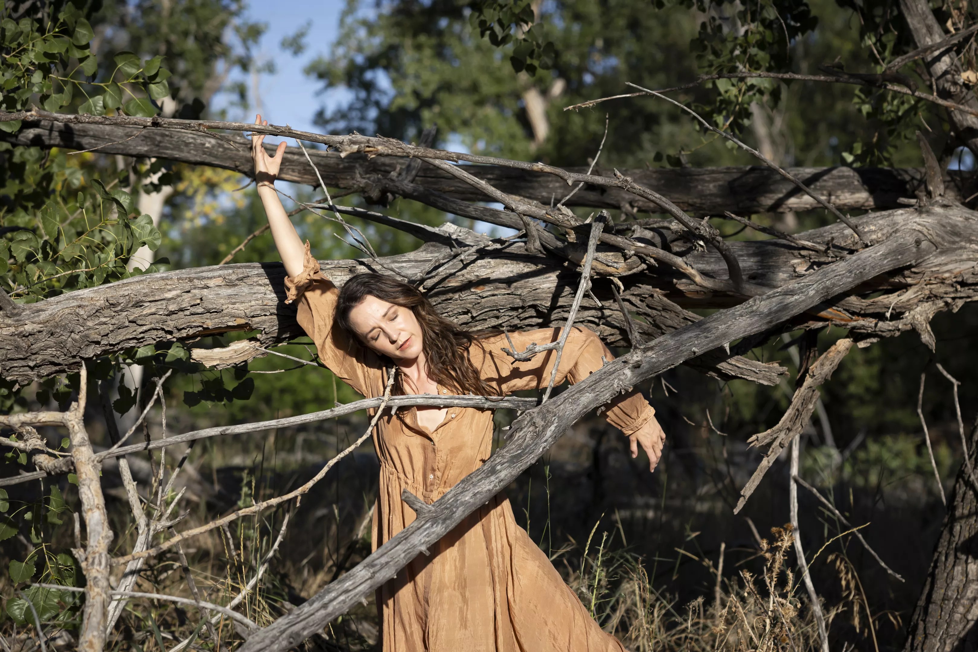 Woman in brown dress standing between branches.