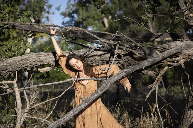 Woman in brown dress standing between branches.
