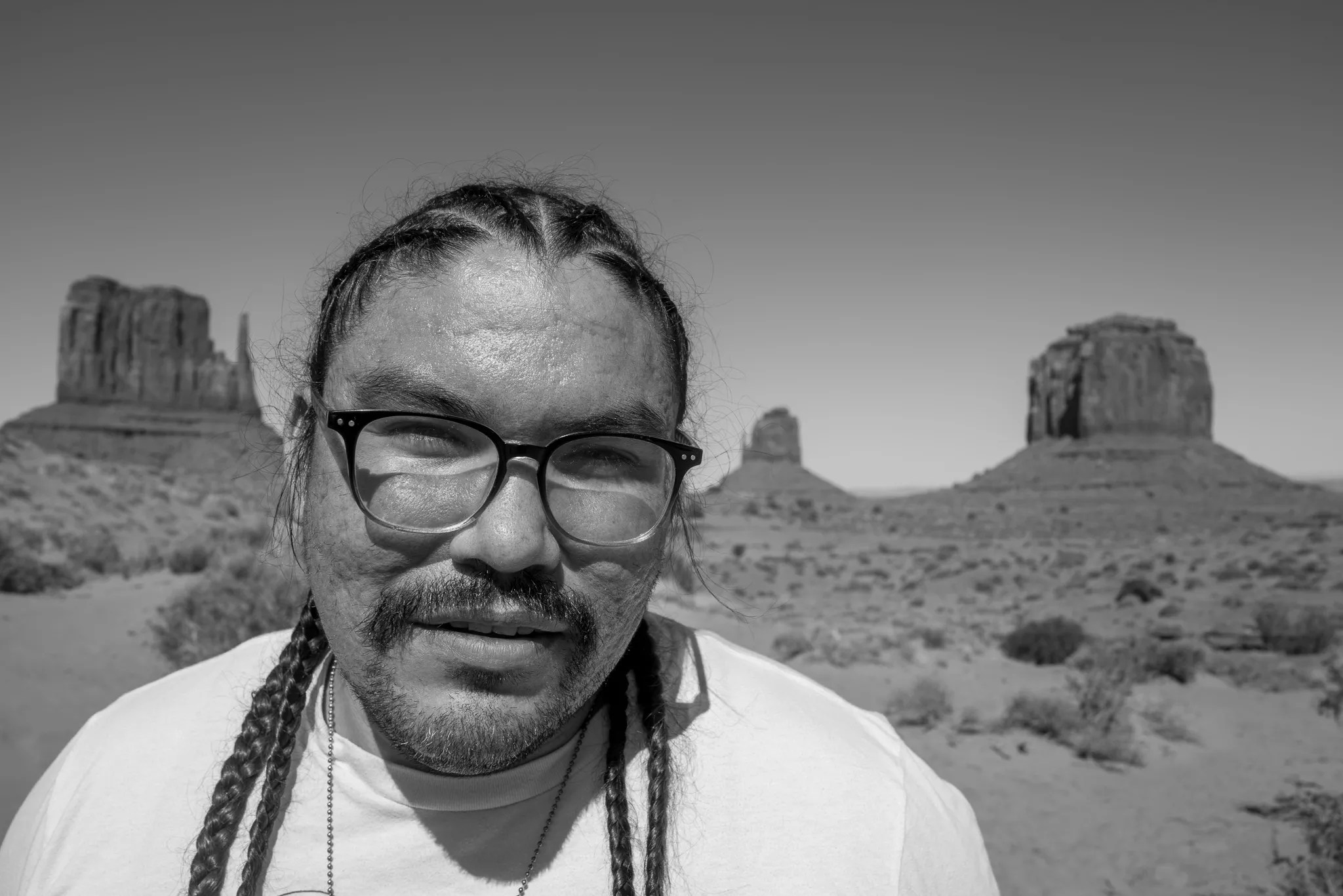 A black-and-white headshot of a man wearing glasses in the desert.