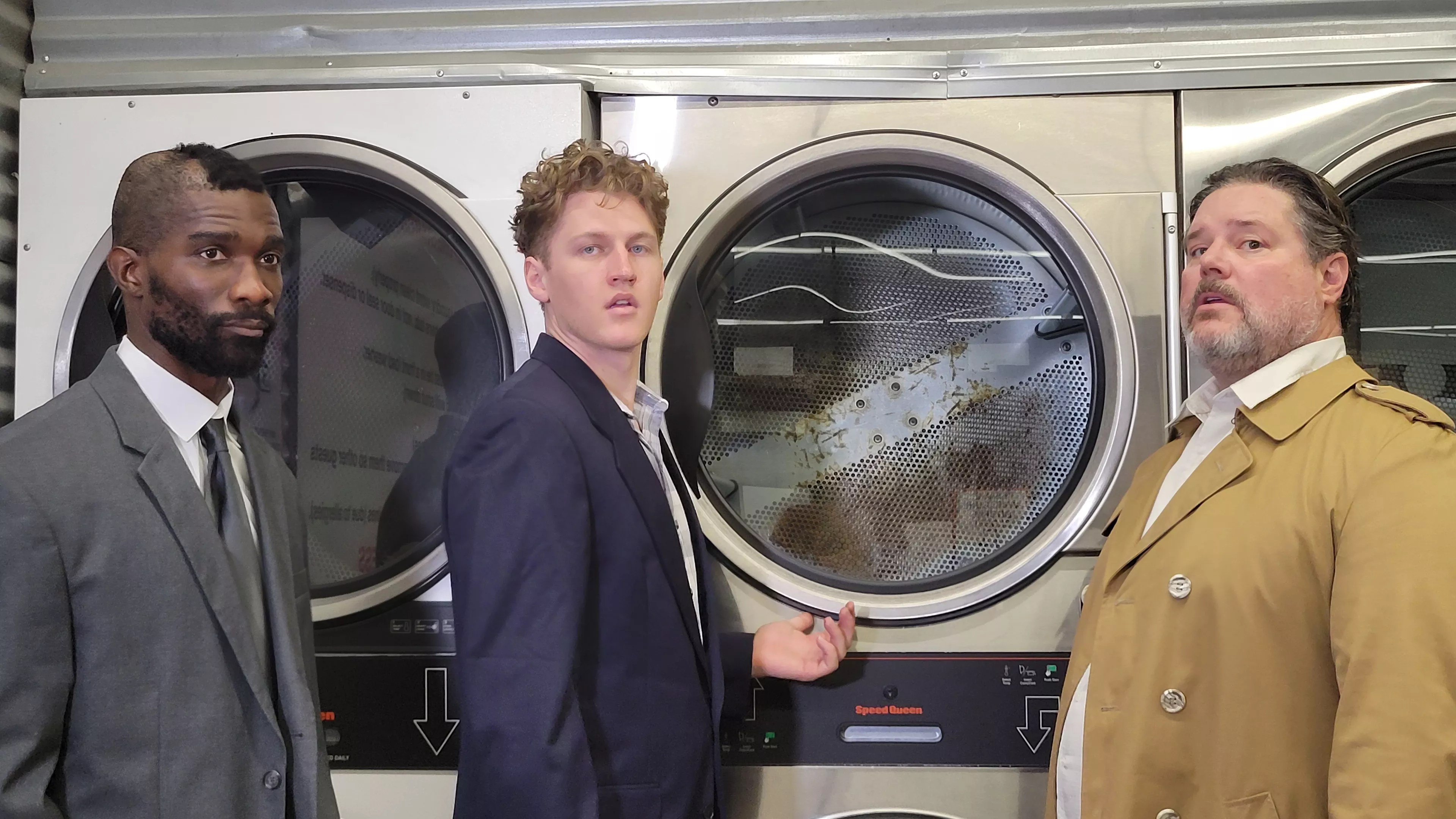 Three men stand in a laundry mat.