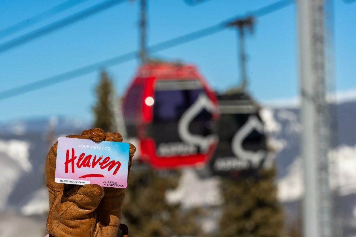A gloved hand holding an Alex Israel-designed lift ticket while backdropped by the Aspen Mountain gondola