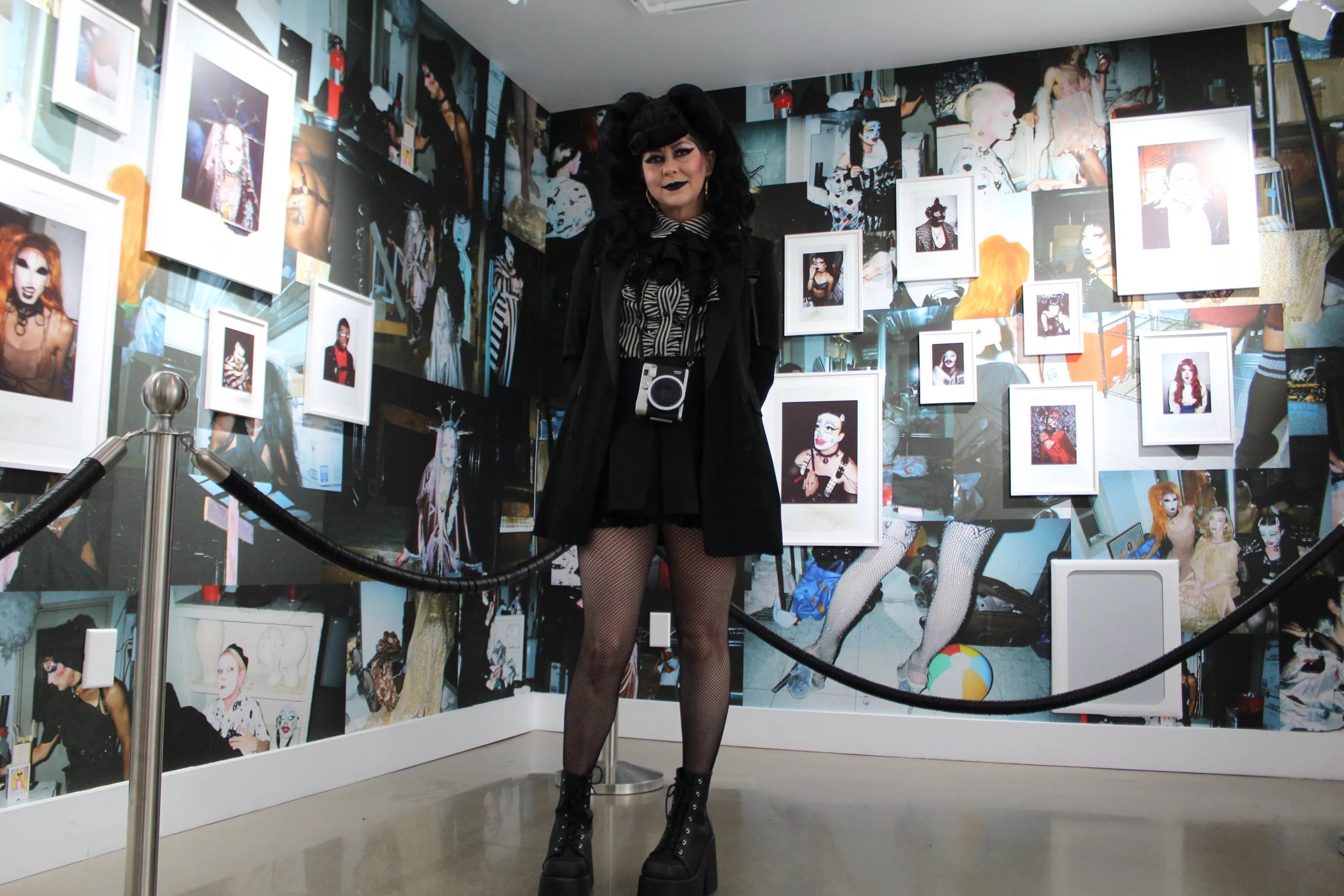 A woman dressed in black stands in front of a wall of photos