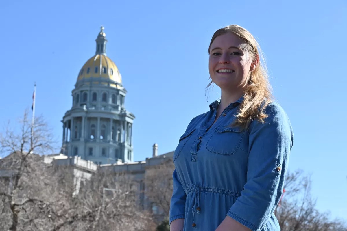 A woman stands in front of the Colorado State Capitol.
