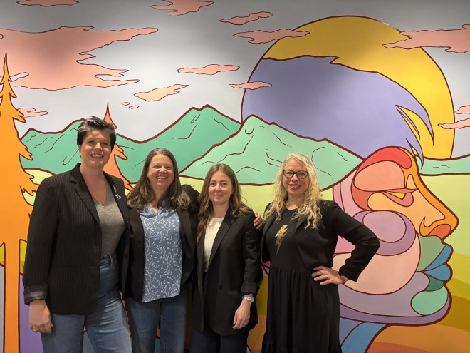 women in blazers smile in front of a mural