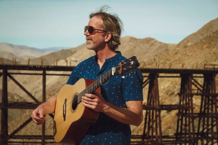 man with a guitar looks at mountains