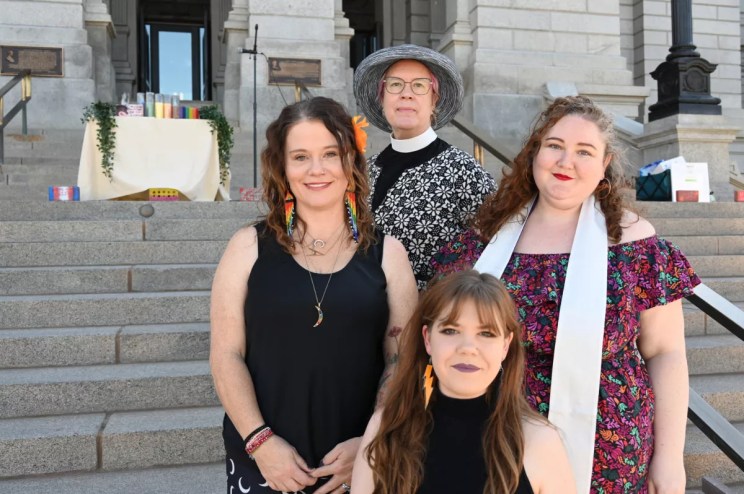 Four women stand in front of the State Capitol west steps.