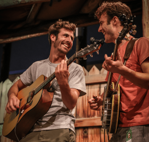 man playing guitar smiles at man playing banjo