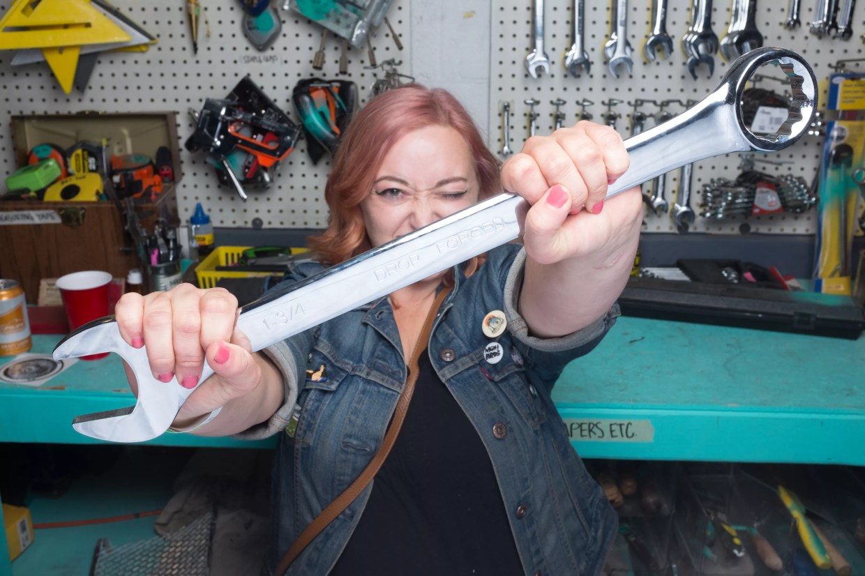 A woman holds a wrench.