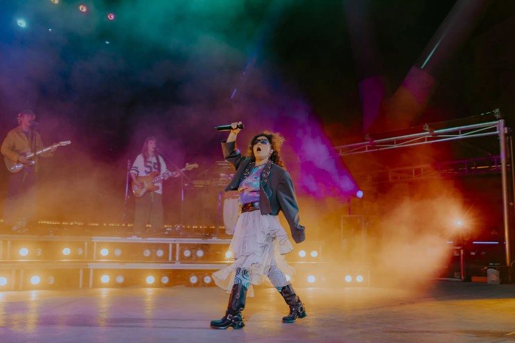 A picture of Remi Wolf performing on stage at Red Rocks with fog and stage lights behind her.