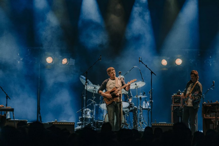 A photo of Sturgill Simpson performing on stage with blue stage lights behind him.