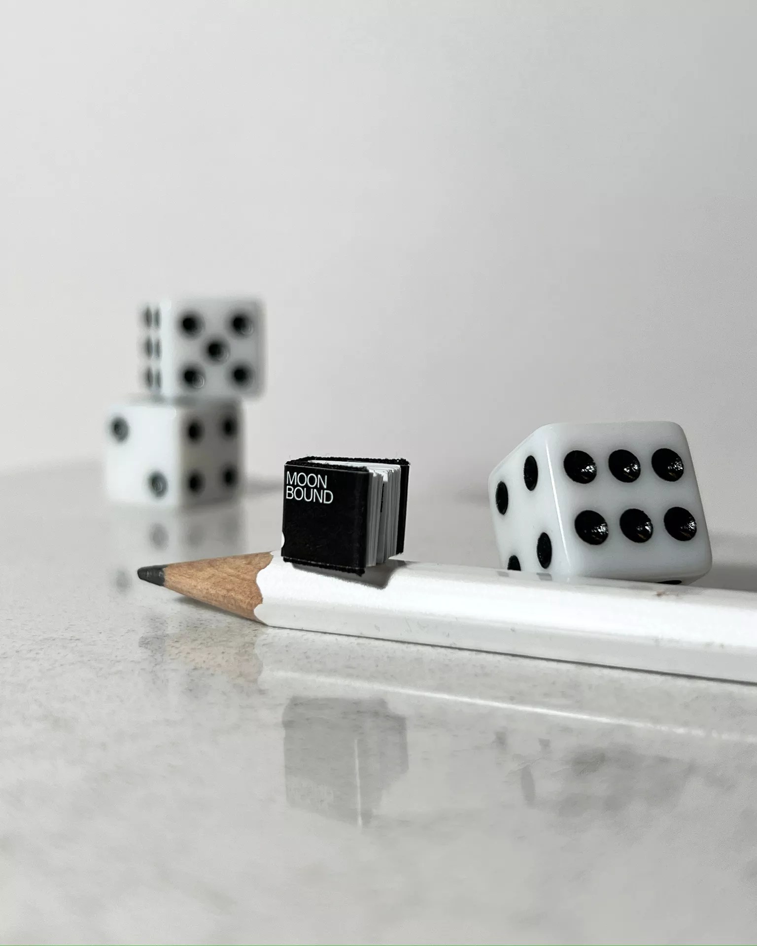 A tiny book with a pencil and dice for comparison