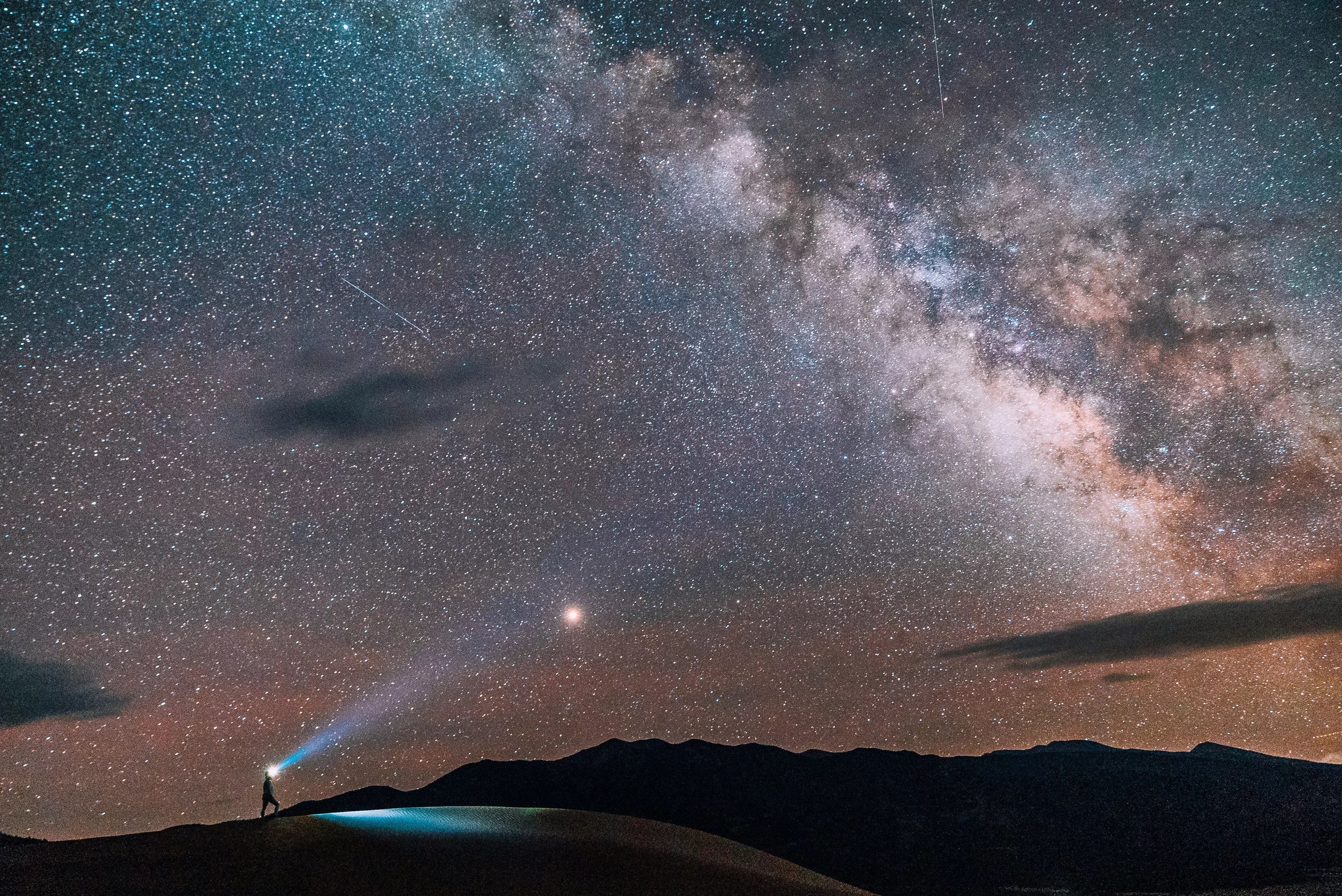 A person wearing a headlamp while hiking beneath the Milky Way at Great Sand Dunes National Park