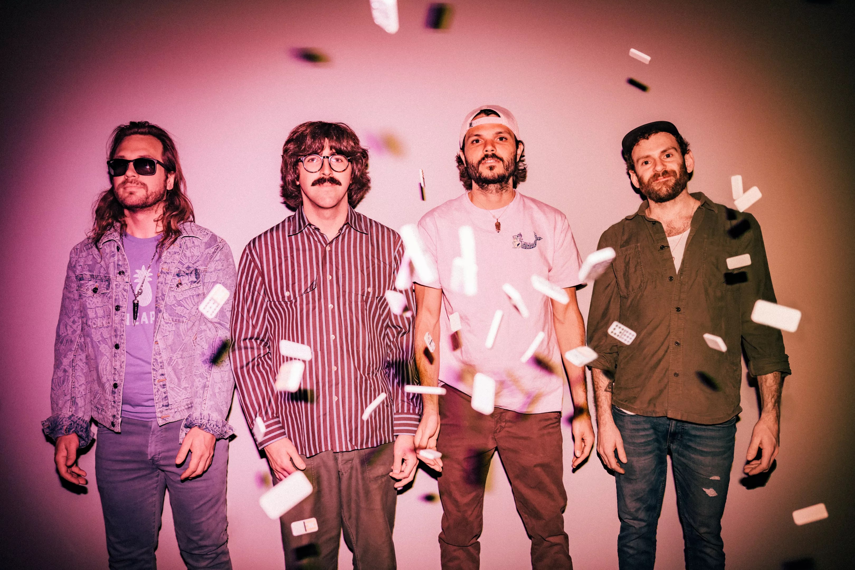 members of the jam band goose stand in pink lighting with confetti