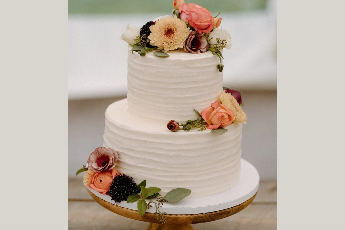 A vegan two-tier wedding cake from The Cake Bar, featuring white frosting and fresh flowers
