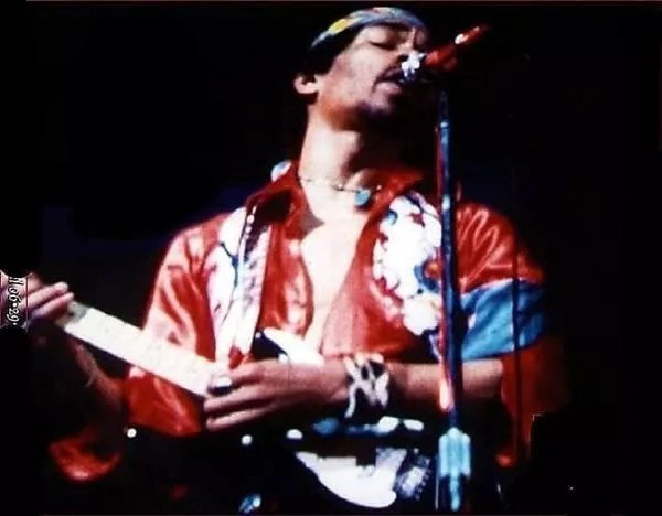 Jimi Hendrix playing guitar in a red silk shirt