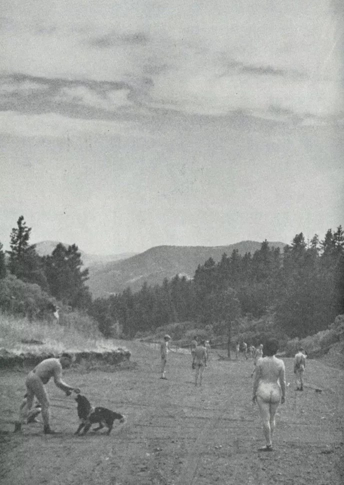 a black and white photo of naked people playing with a dog