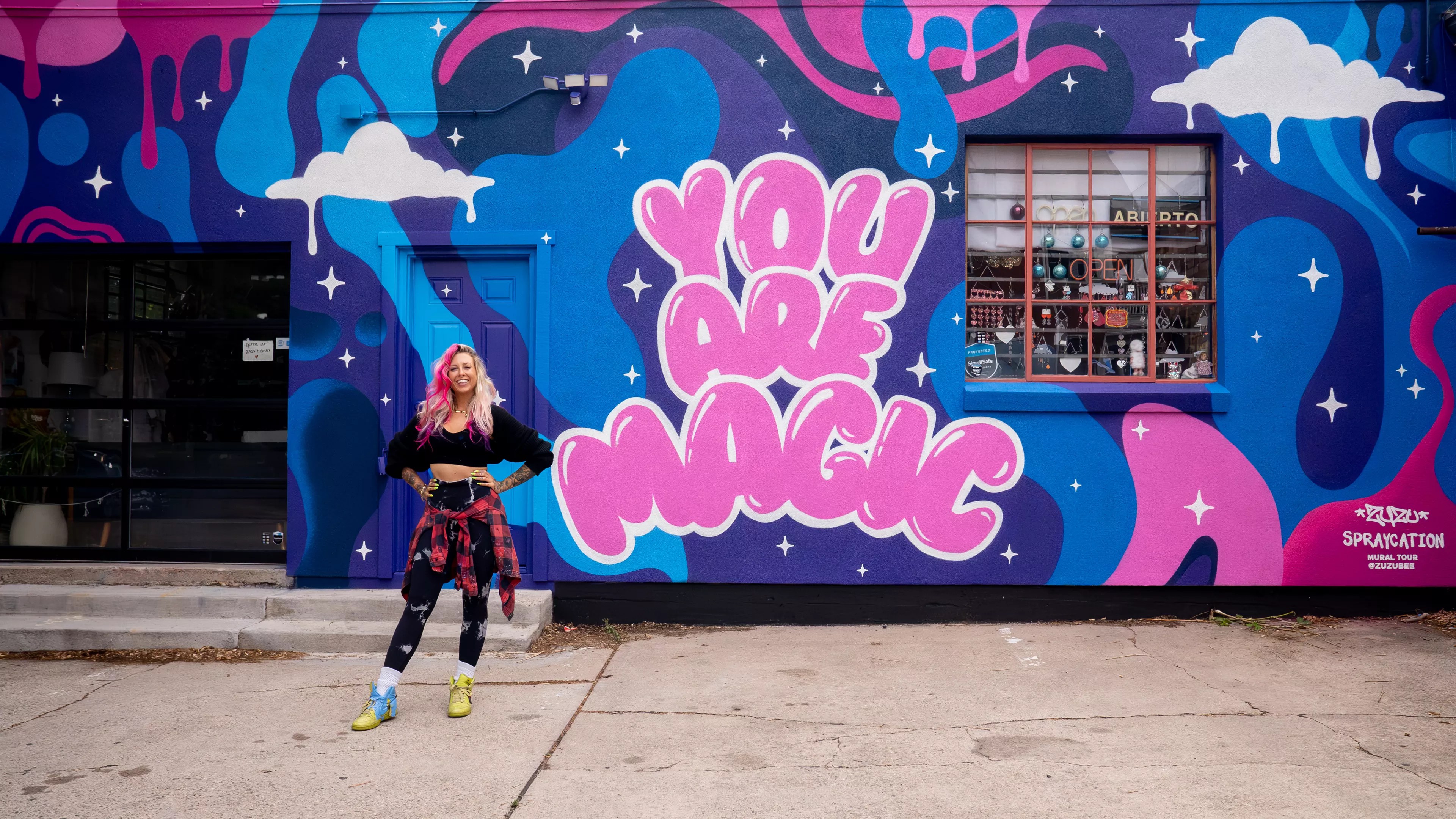 a woman stands in front of a colorful mural