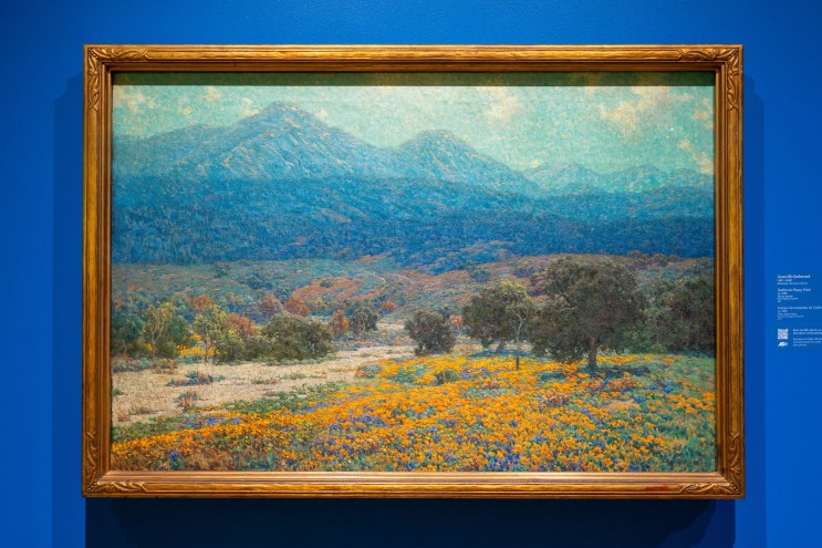 A colorful painting of a landscape against a blue wall