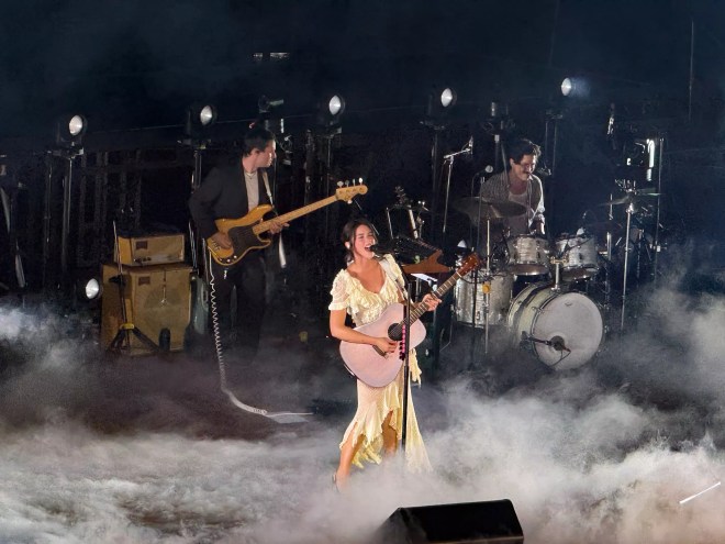 Gracie Abrams performing with a guitar on stage with her band.