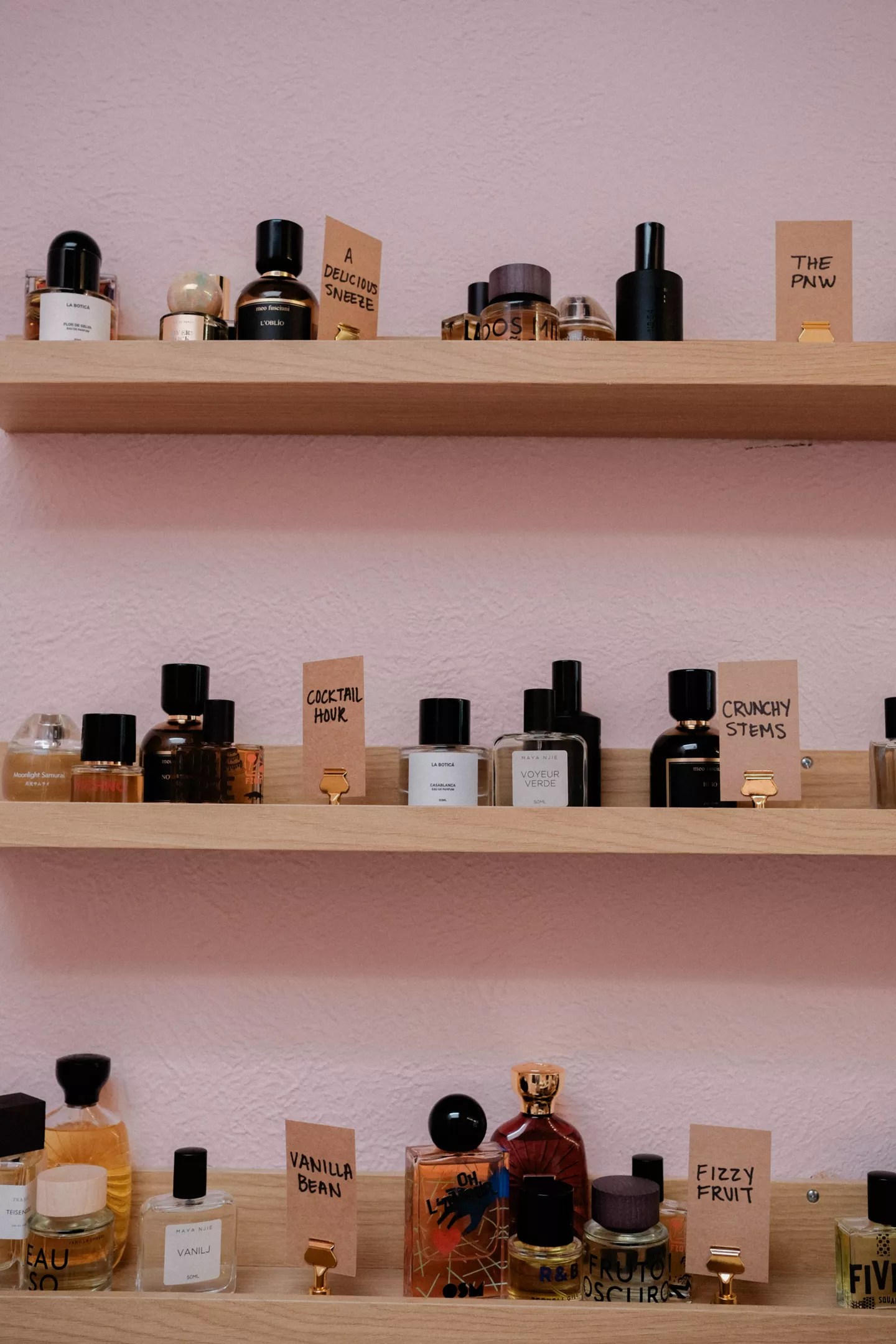 A pink wall with shelves of perfume bottles